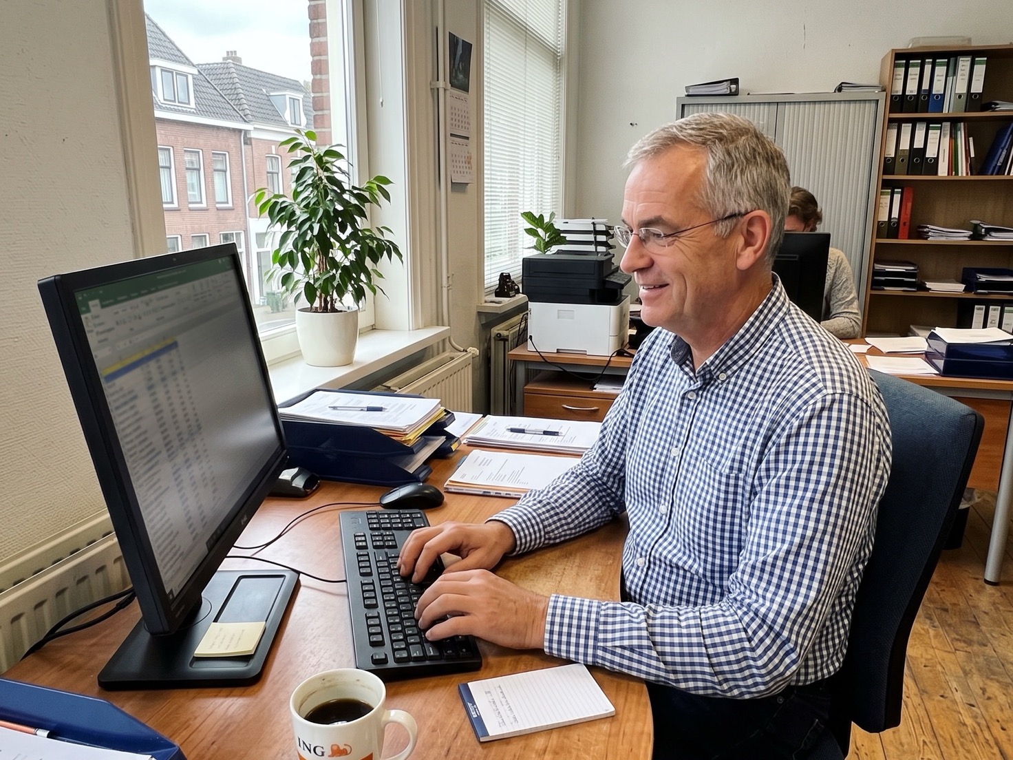 Adviseur van opzij gefotografeerd, typend aan zijn bureau bij het raam van een rustig advieskantoor