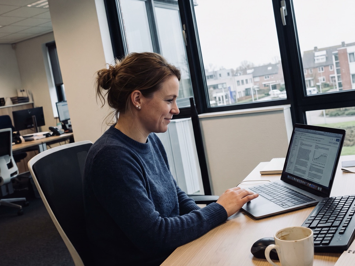 Adviseur achter haar laptop in een advieskantoor, bezig met een artikel op het scherm