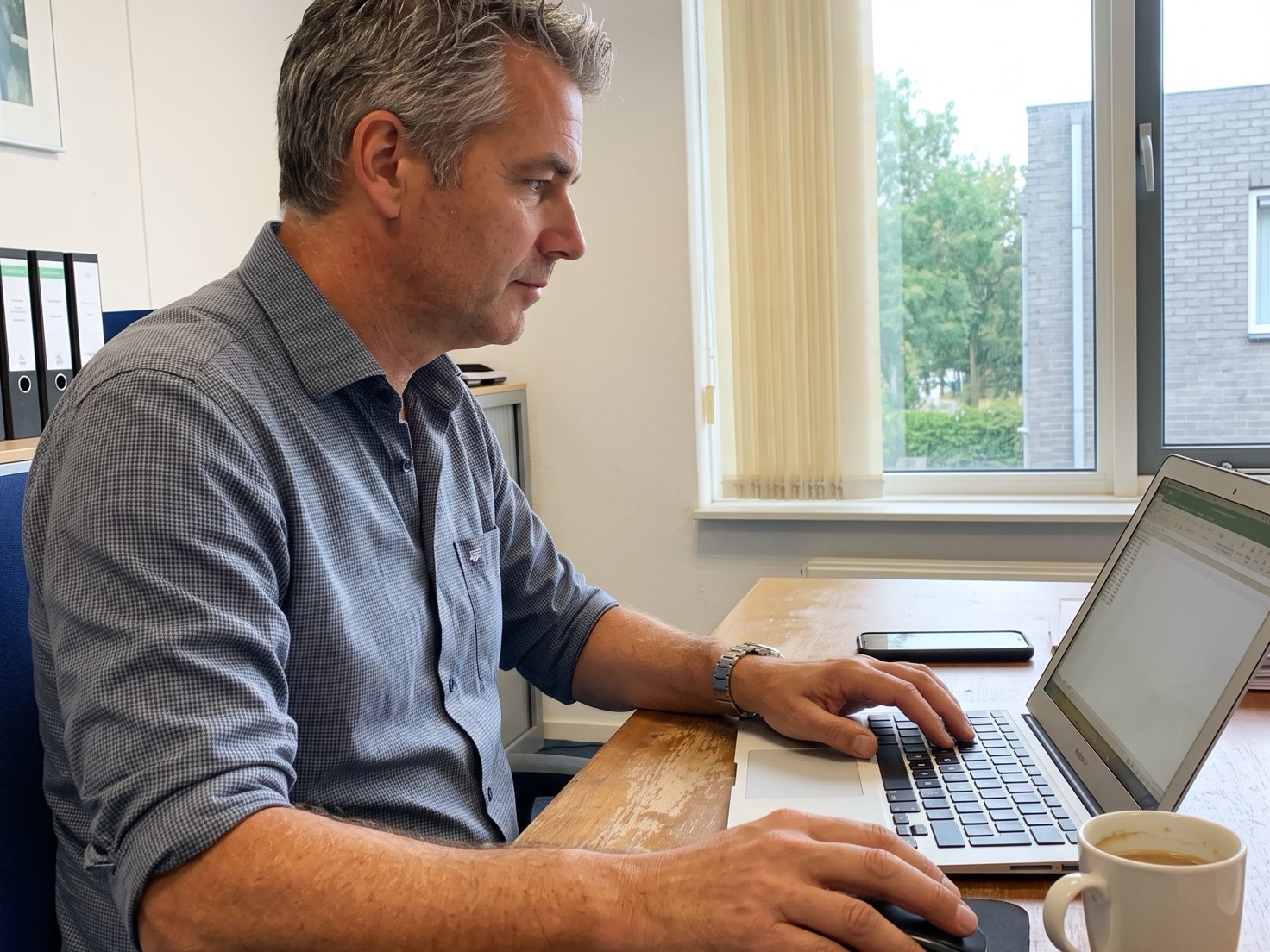 Adviseur werkt over de schouder gefotografeerd achter zijn laptop in een rustig advieskantoor