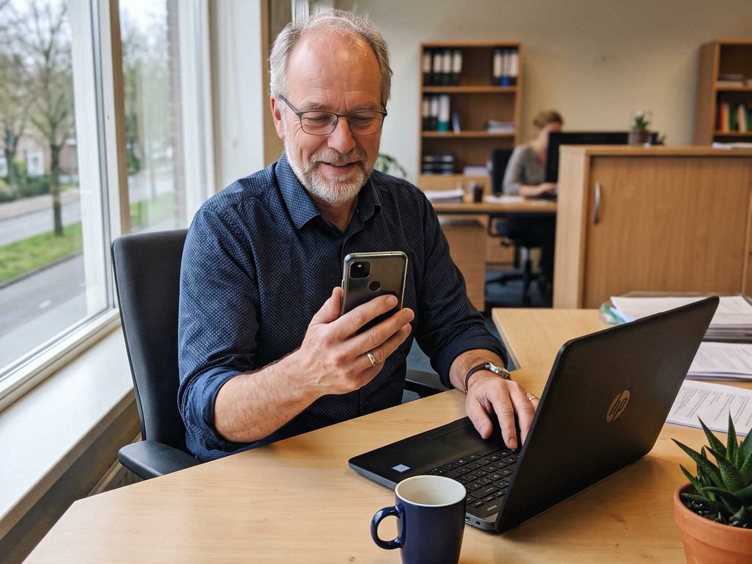 Adviseur bekijkt zijn telefoon achter zijn bureau in een rustig advieskantoor