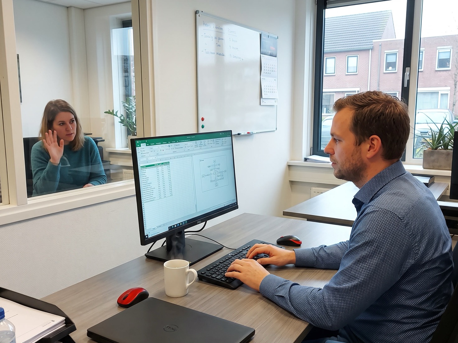 Financieel adviseur werkt aan zijn bureau in een Nederlands advieskantoor, een collega zwaait vanuit de kamer ernaast