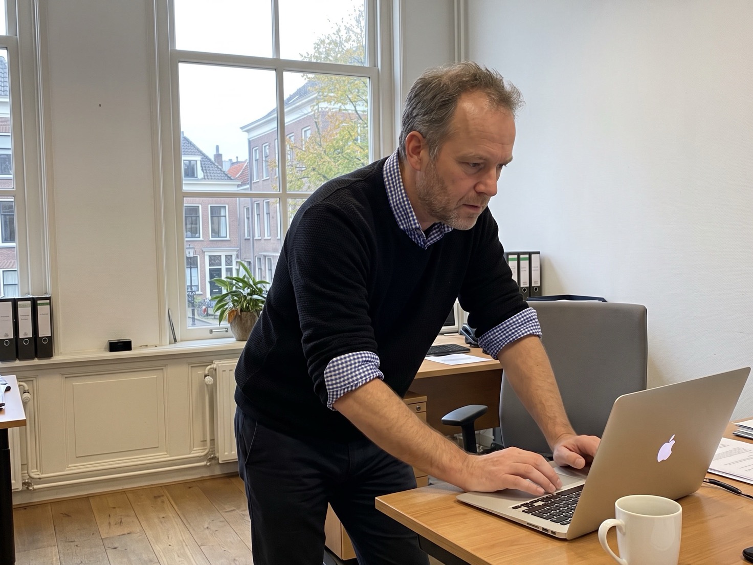 Financieel adviseur typt achter zijn bureau in een rustig advieskantoor, scherm van de camera af