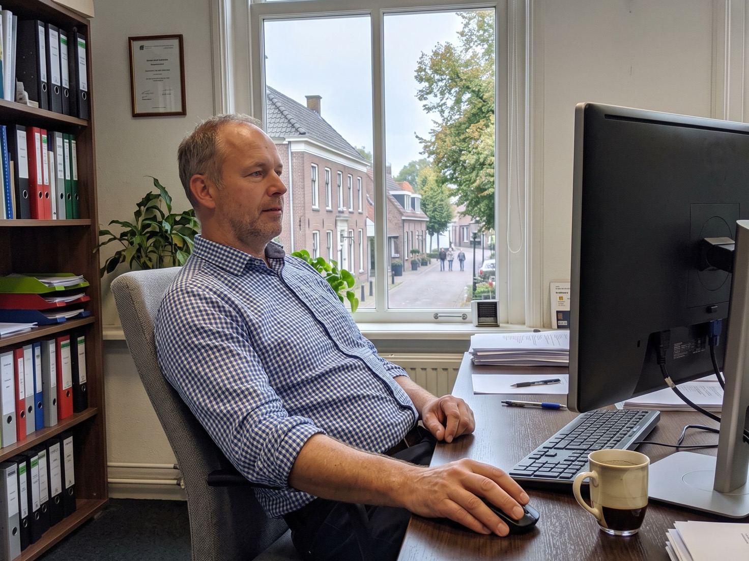 Adviseur leunt achterover aan zijn bureau in een rustig advieskantoor, blik op het scherm
