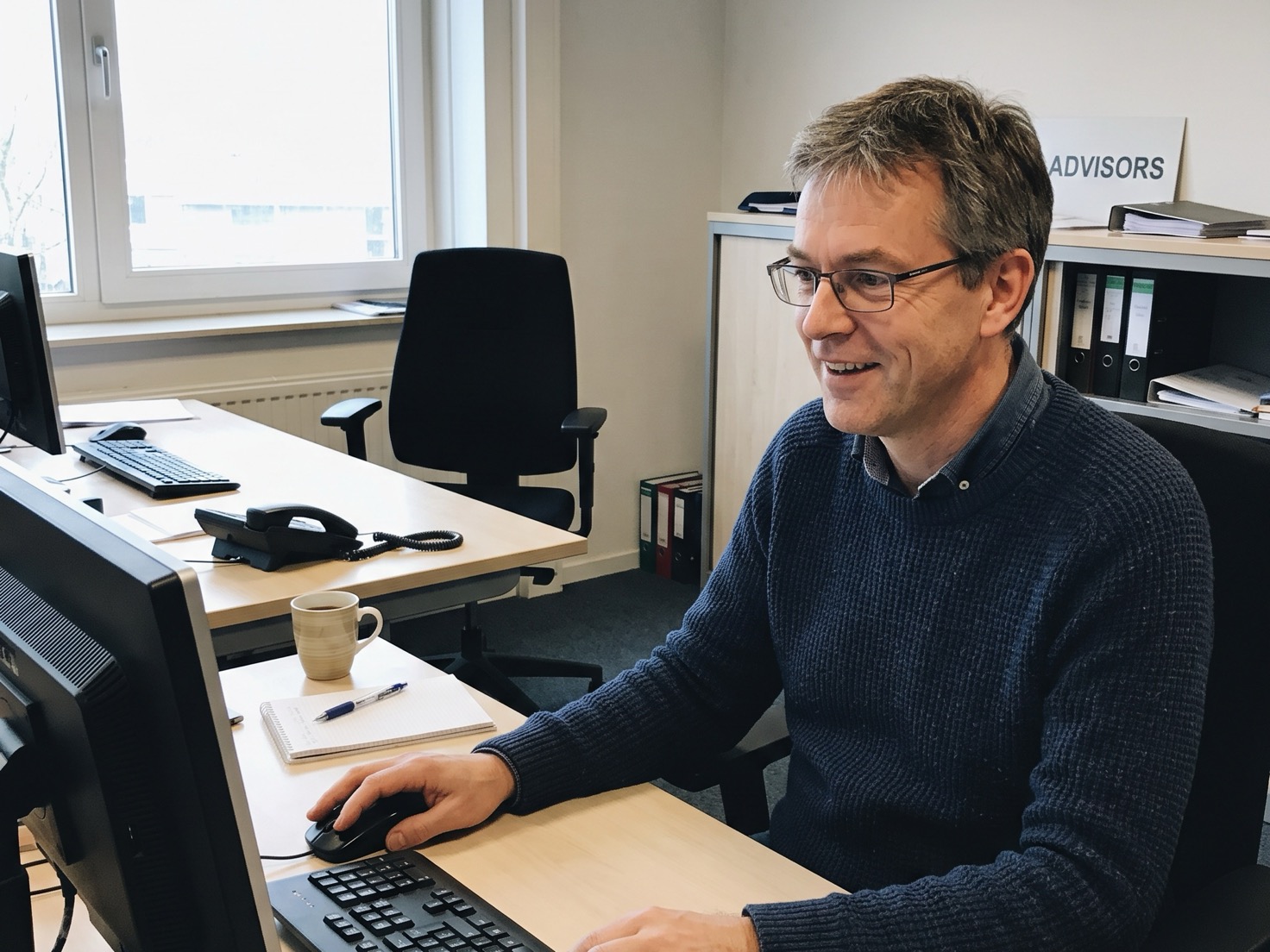 Financieel adviseur achter zijn bureau zoekt op zijn computer een eerder verstuurde nieuwsbrief terug