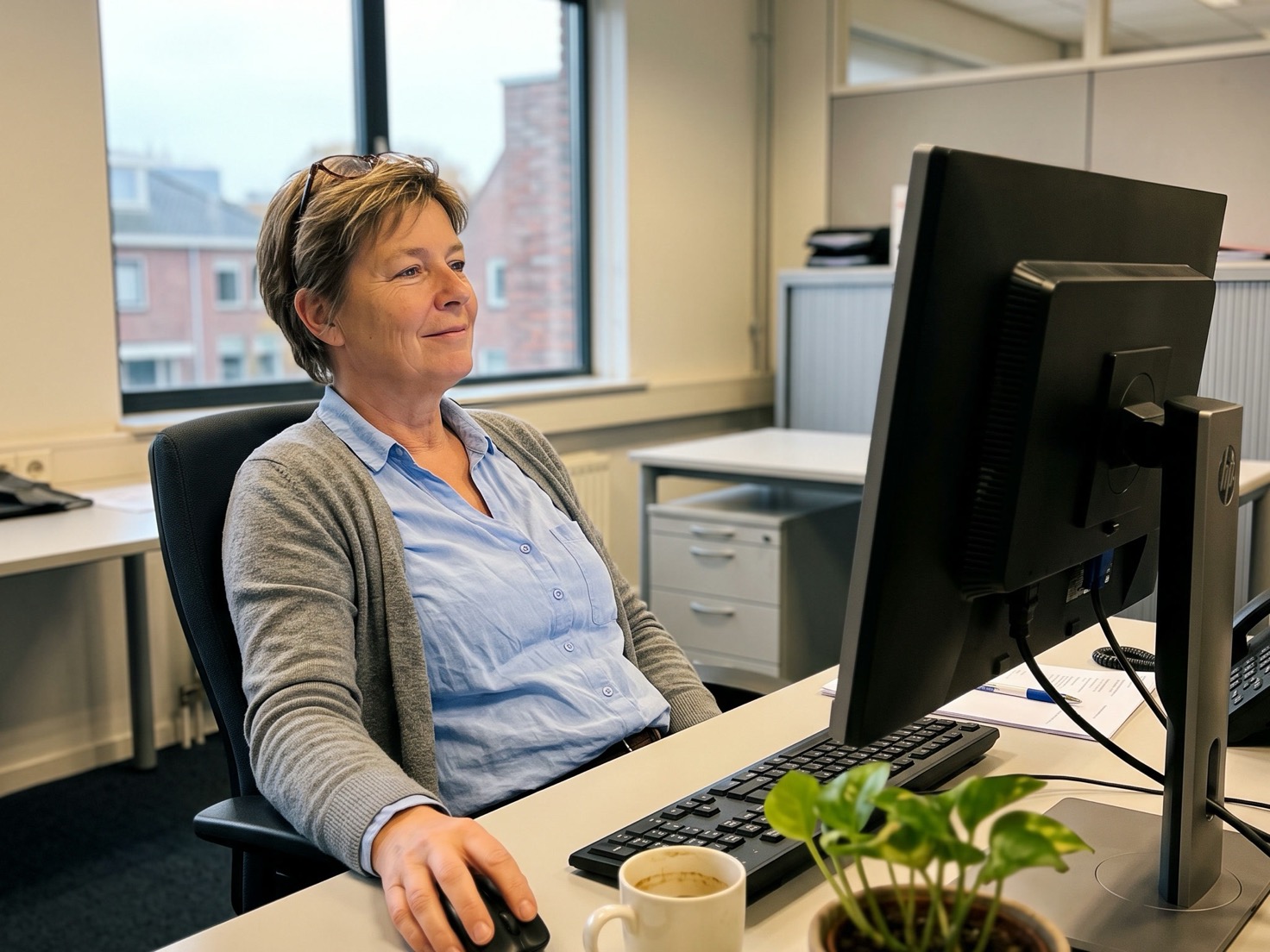 Accountant op een licht kantoor die tevreden naar haar beeldscherm kijkt terwijl ze de nieuwsbrief van deze maand nakijkt