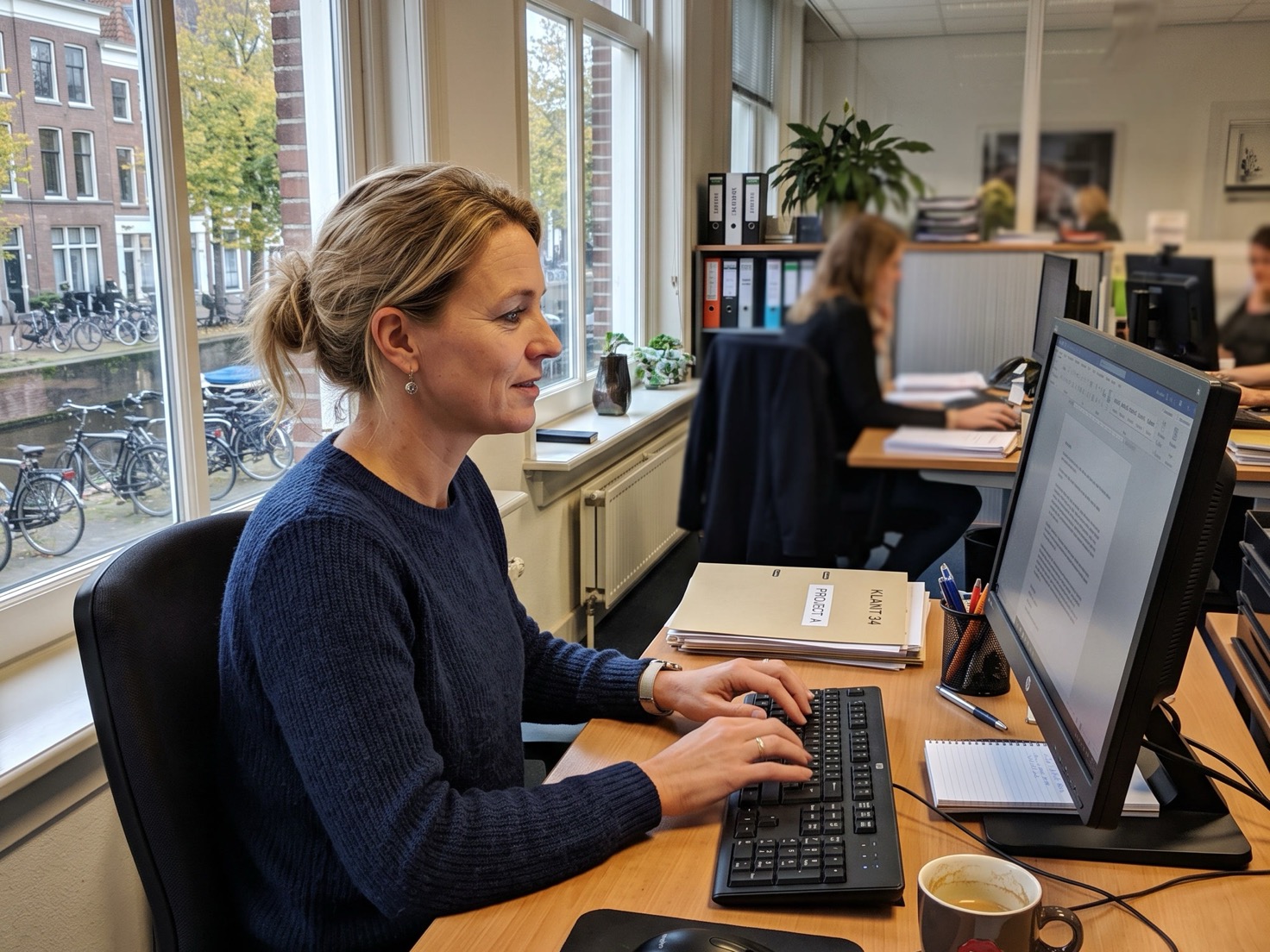 Financieel adviseur schrijft een kennisbank-artikel achter haar bureau bij het raam