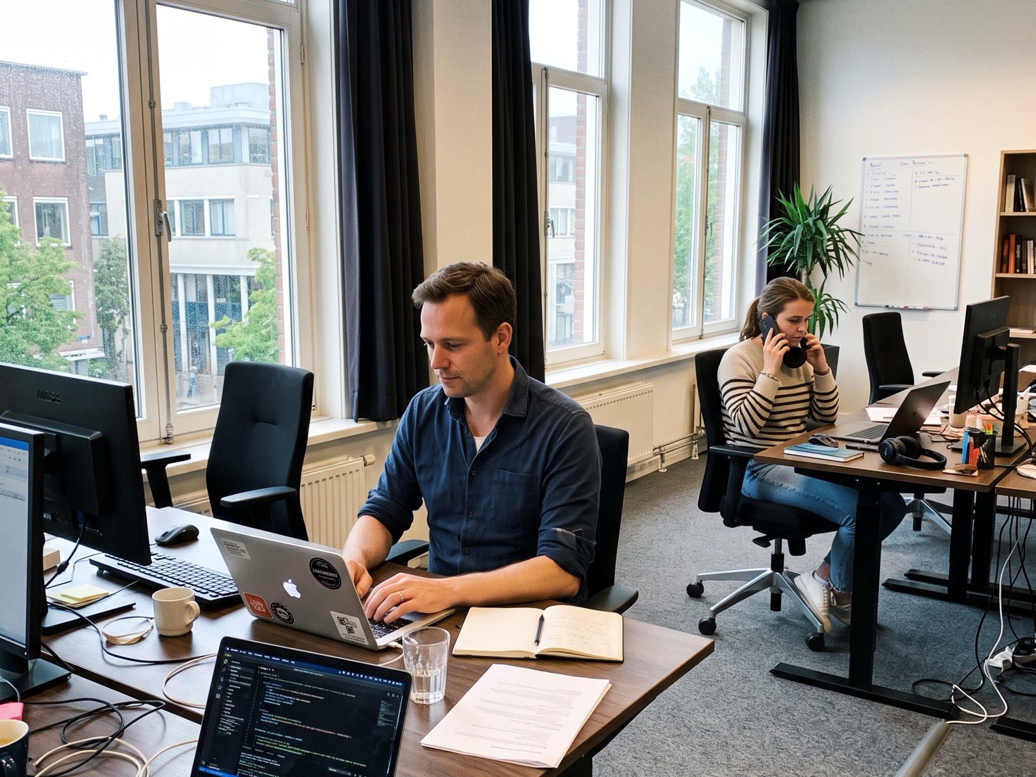Financieel adviseur werkt achter zijn bureau terwijl een collega achterin het kantoor een videogesprek afrondt.