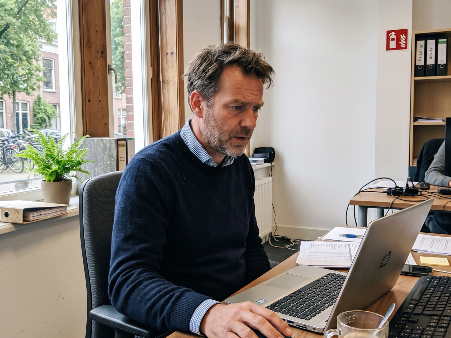 Adviseur werkt achter zijn laptop in een rustig advieskantoor met een kopje koffie op het bureau