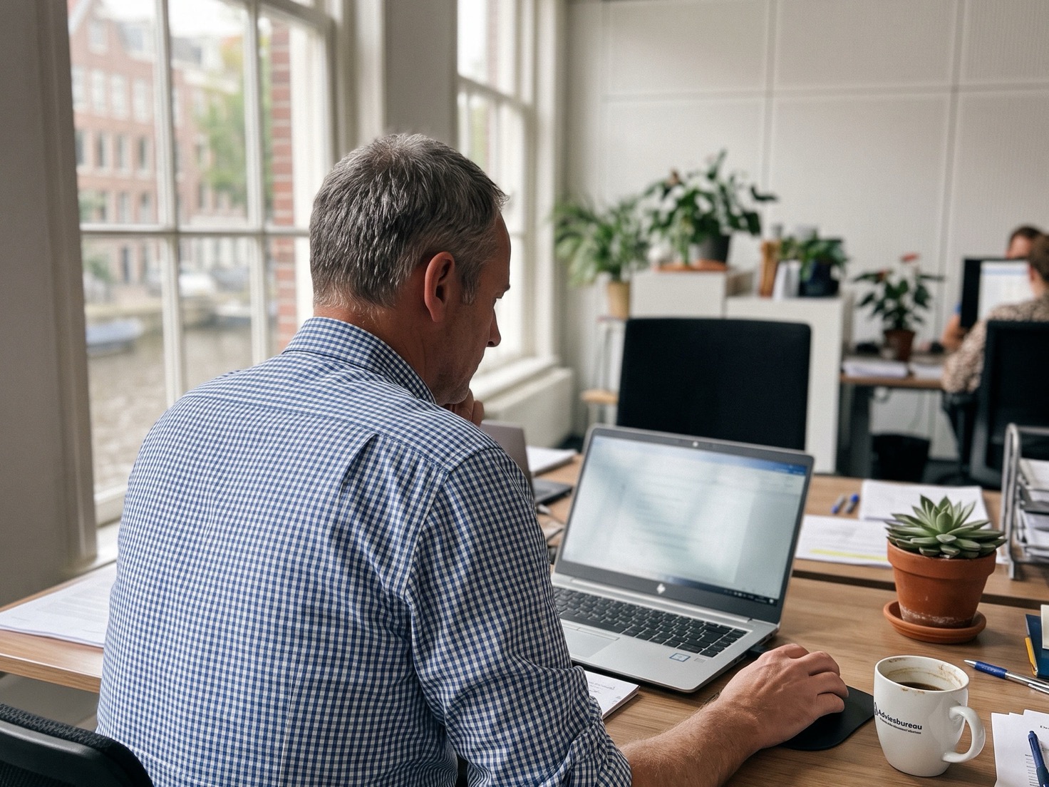 Adviseur werkt geconcentreerd achter zijn laptop in een Nederlands advieskantoor